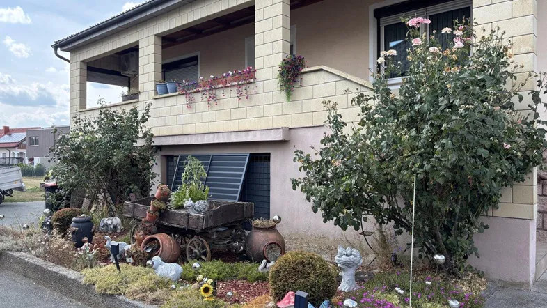 Vorgarten mit dekorativen Elementen und Blumenbeeten vor dem Haus mit Balkon.