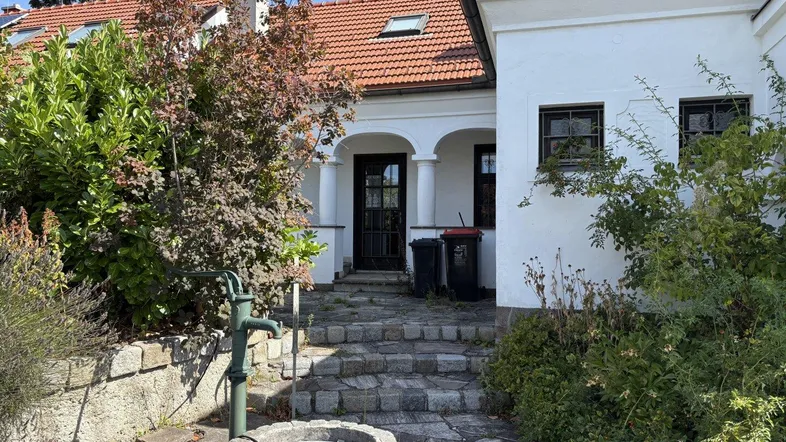 Eingangsbereich eines charmanten Hauses mit Steintreppe, Garten und traditionellem Brunnen.