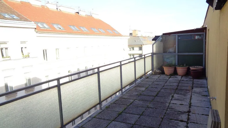 Geräumige Terrasse mit Fliesenboden, Metallgeländer und Blick auf umliegende Gebäude.