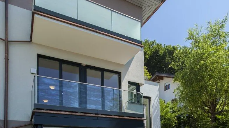 Moderne Architektur mit Balkonen, einer Holzterrasse und einem kleinen Gartenhaus im Grünen.