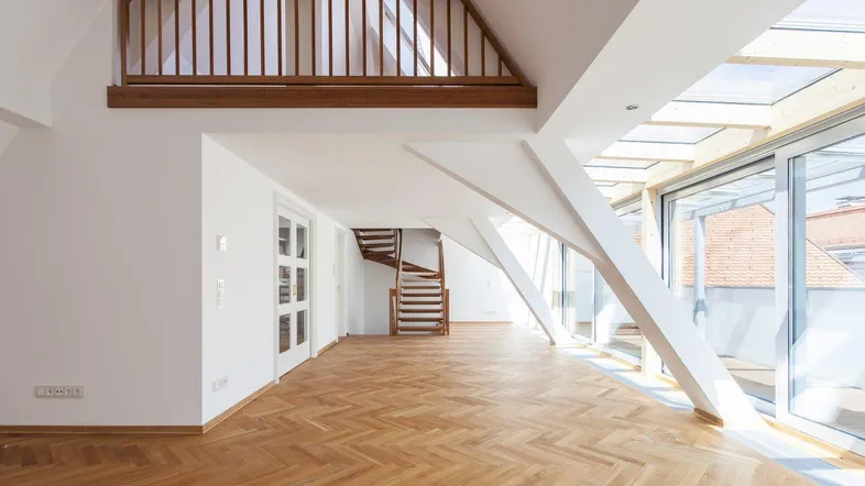 Helles, offenes Wohnzimmer mit Fischgrätparkett, hohen Decken und Zugang zu einer Galerie.
