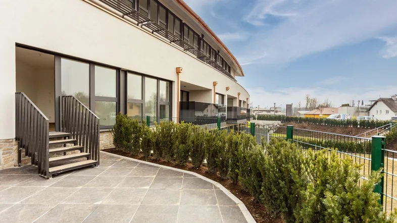 Moderne Gebäudefassade mit großer gepflasterter Terrasse und Zugang zu den Wohnungen.