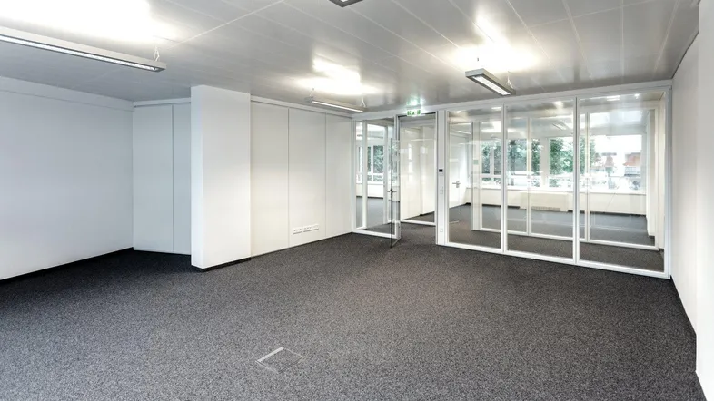 Geräumiges Büro mit Teppichboden und Glaswänden, die separate Arbeitsbereiche schaffen.