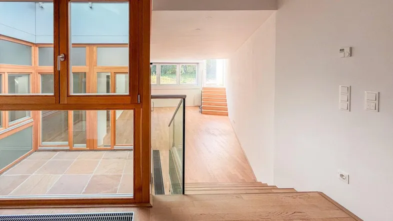 Heller Übergangsbereich mit Holzfenstern, Glasgeländer und Blick in den Innenhof.