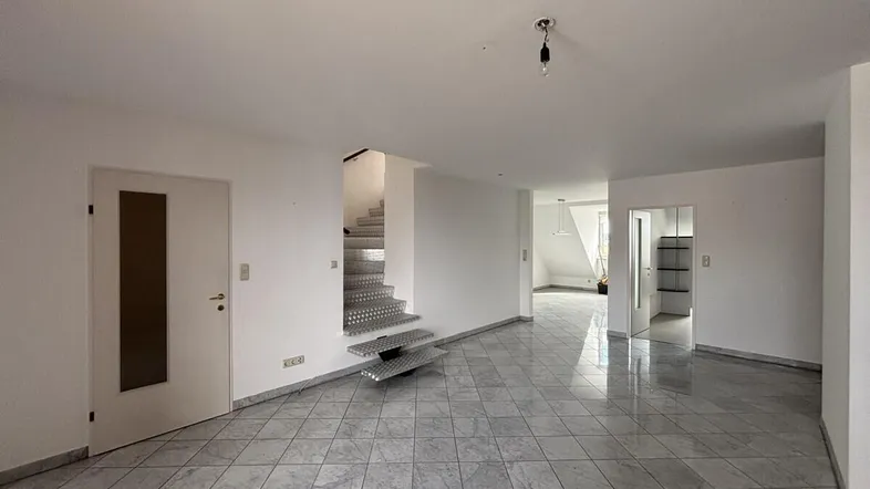 Geräumiger Wohnbereich mit hellen Fliesen, einer modernen Metalltreppe und Zugang zu weiteren Räumen.
