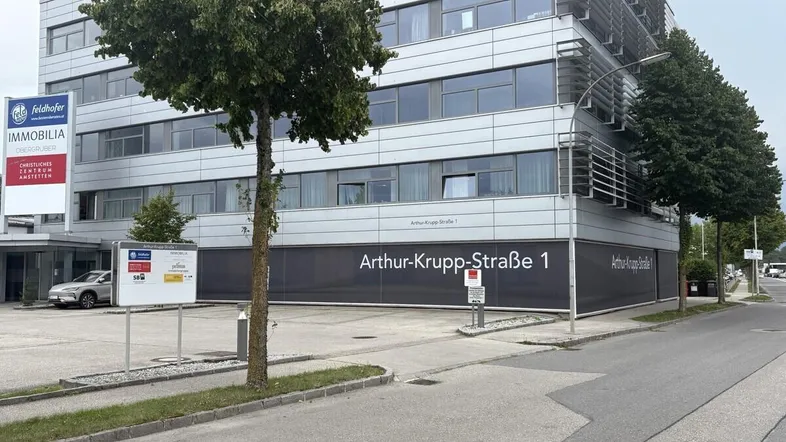 Modernes Bürogebäude mit Glasfassade und Parkplätzen an der Straße.