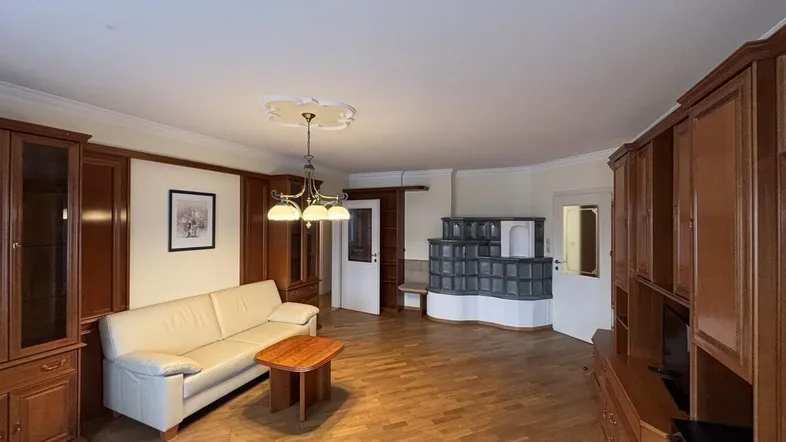 Geräumiges Wohnzimmer mit traditionellem Kachelofen, Parkettboden und Holzmöbeln.