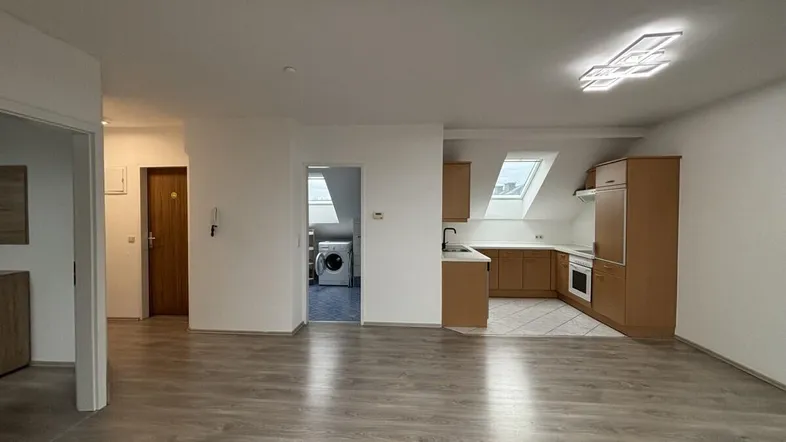 Geräumiger offener Wohnbereich mit Laminatboden, Dachschrägen und angrenzender Küche.