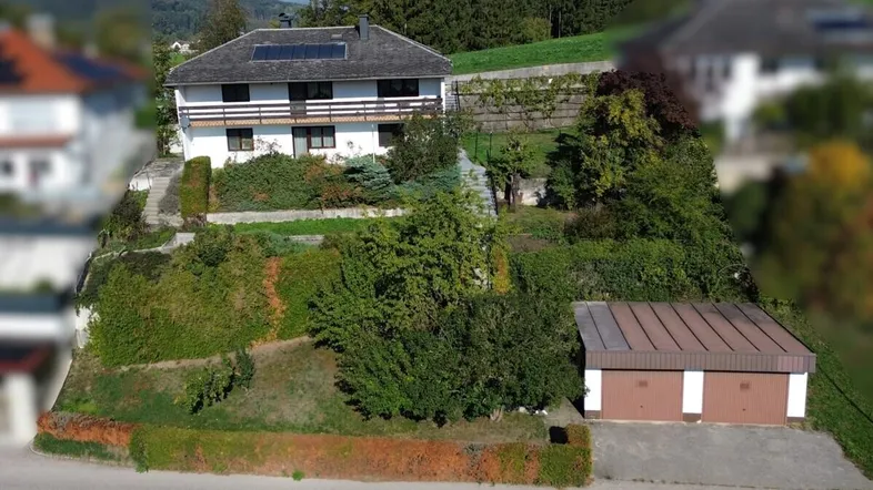 Freistehendes Haus mit Photovoltaikanlage auf dem Dach, umgeben von terrassierten Gärten und einer Doppelgarage.