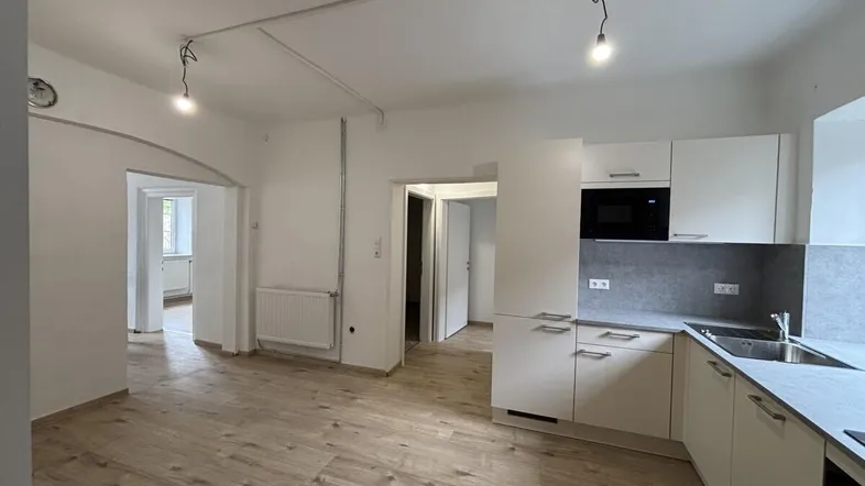Helle, offene Küche mit weißen Schränken, grauer Arbeitsplatte und Holzfußboden in einem kombinierten Wohnbereich.