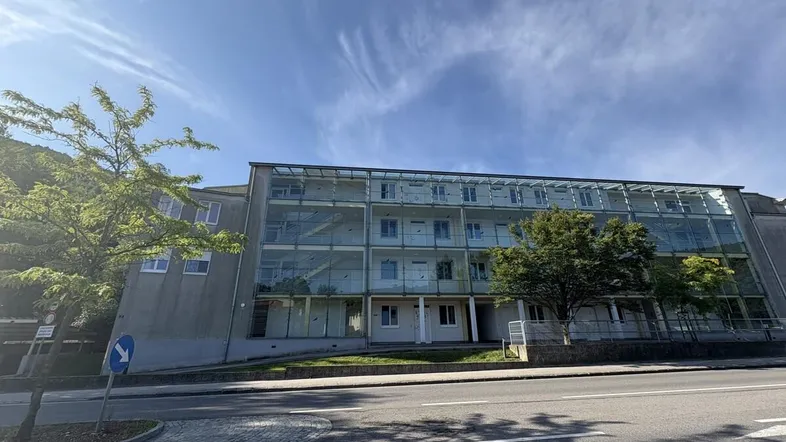 Moderne Gebäudefassade mit großen Glasflächen und Balkonen, direkt an einer Straße gelegen.
