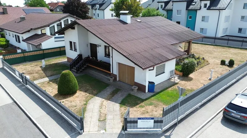 Einfamilienhaus mit braunem Satteldach, weißer Fassade und großem Gartenbereich in ländlicher Umgebung.