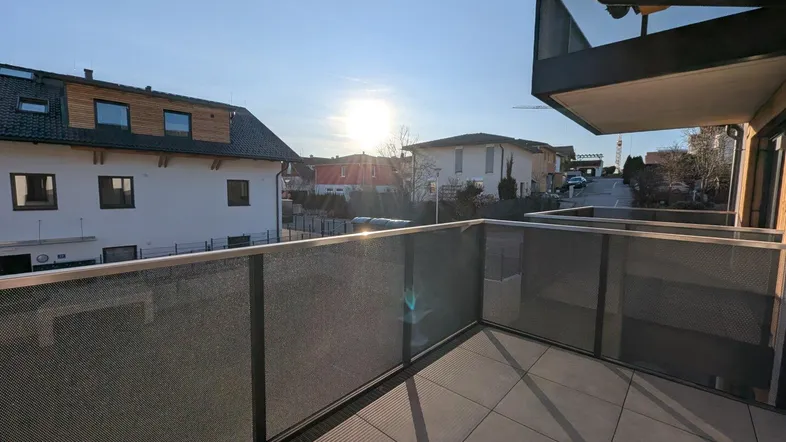 Geräumiger Balkon mit Fliesenboden und Glasgeländer, bietet einen schönen Blick auf die Umgebung bei Sonnenuntergang.