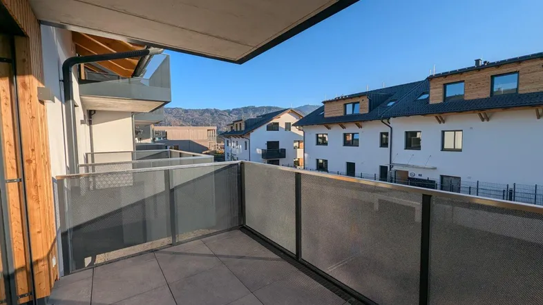 Heller Balkon mit Fliesenboden und moderner Metallbrüstung, bietet Blick auf die umliegenden Häuser und Berge.