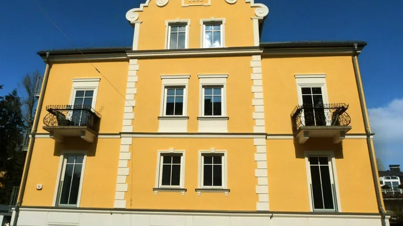 Vorderansicht eines historischen Gebäudes von 1893 mit gelber Fassade und dekorativen Balkonen.
