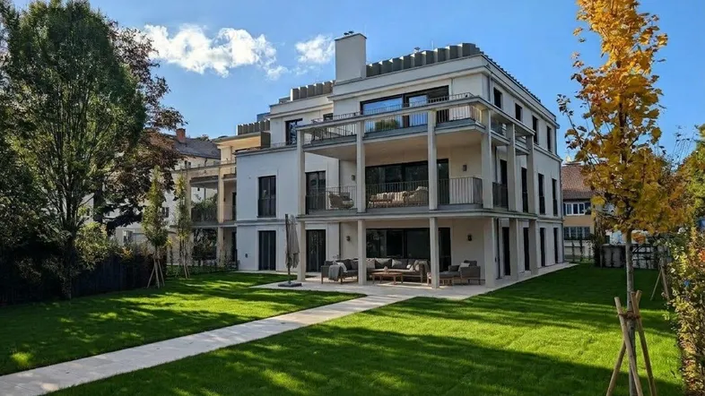 Modernes Mehrfamilienhaus mit großzügigen Balkonen, Terrassen und gepflegter Grünfläche unter blauem Himmel.