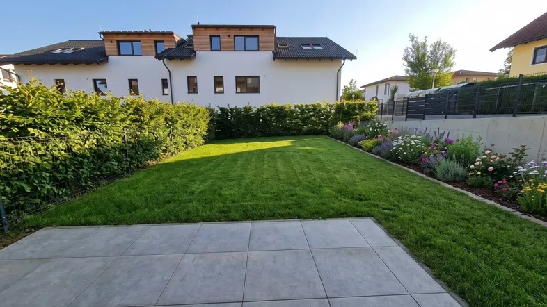 Große Terrasse mit Rasenfläche und Hecke, umgeben von einem gepflegten Gartenbereich.