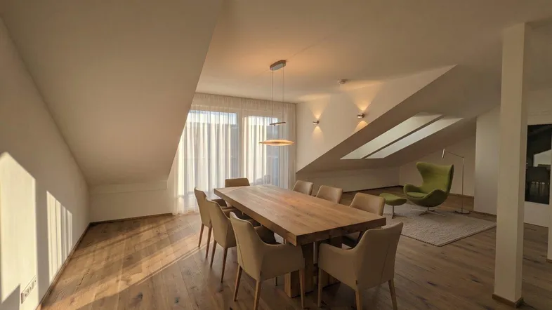 Geräumiger Wohn- und Essbereich mit Holzboden, Dachschrägen und großen Fenstern für viel Tageslicht.