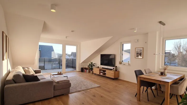 Helles und offenes Wohn-Esszimmer mit Holzboden, Dachschrägen und Zugang zum Balkon.