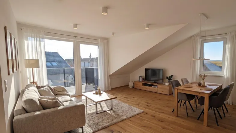 Helles Wohn- und Esszimmer mit Holzboden, Dachschräge und Zugang zu einem Balkon, als Gestaltungsvorschlag.