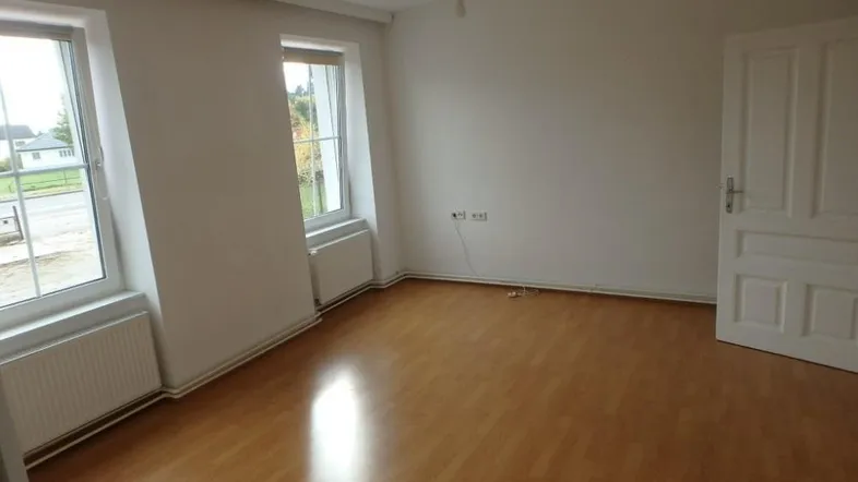 Helles Zimmer mit Laminatboden und zwei Fenstern, ideal als Wohn- oder Schlafzimmer nutzbar.