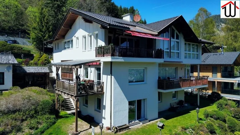 Mehrstöckiges Haus mit mehreren Balkonen und Terrassen in alpiner Umgebung.