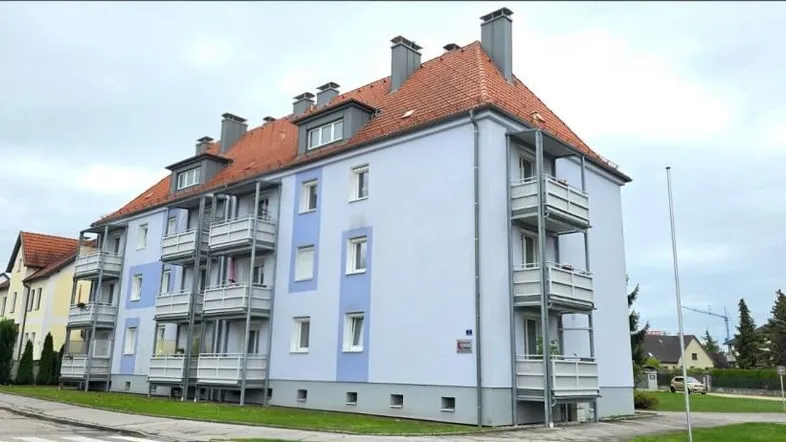 Mehrfamilienhaus mit hellblauer Fassade, roten Ziegeldächern und mehreren Balkonen.