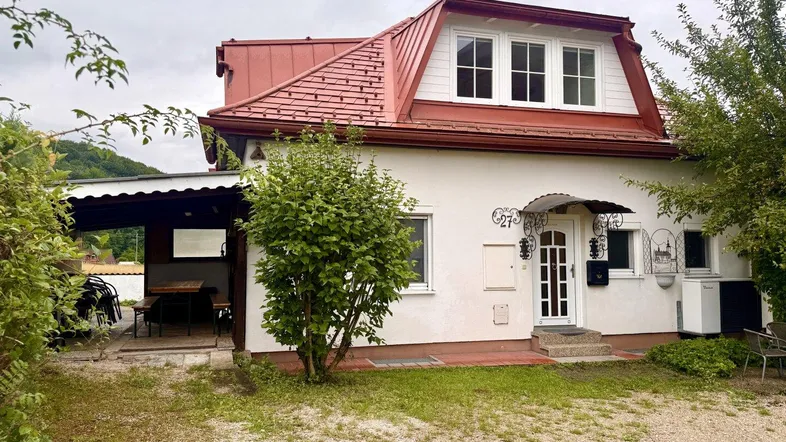Charmantes Einfamilienhaus mit rotem Dach, weißer Fassade und überdachtem Außenbereich im Grünen.