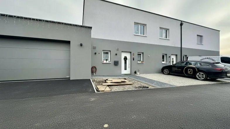 Vorderansicht eines modernen Reihenhauses mit Garage, Stellplatz und gepflegter Zufahrt.
