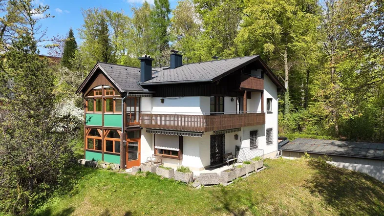 Freistehendes Haus mit Balkon und Wintergarten, umgeben von viel Grün und Bäumen.