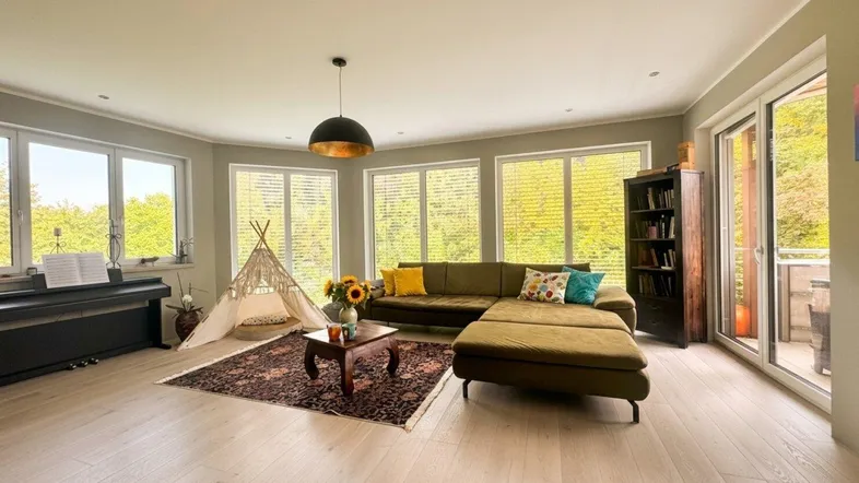 Helles Wohnzimmer mit großem Ecksofa, hellem Holzboden und Zugang zum Balkon.