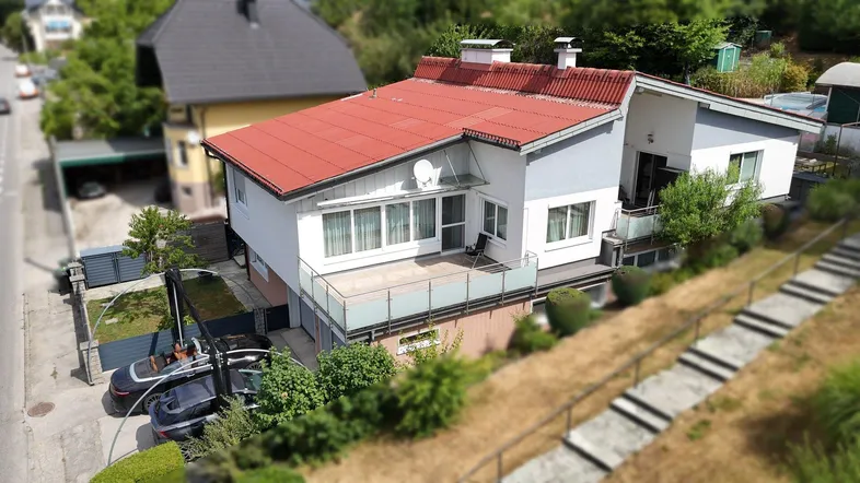 Luftaufnahme des Hauses mit rotem Dach, weißer Fassade, kleinem Balkon und Carport.