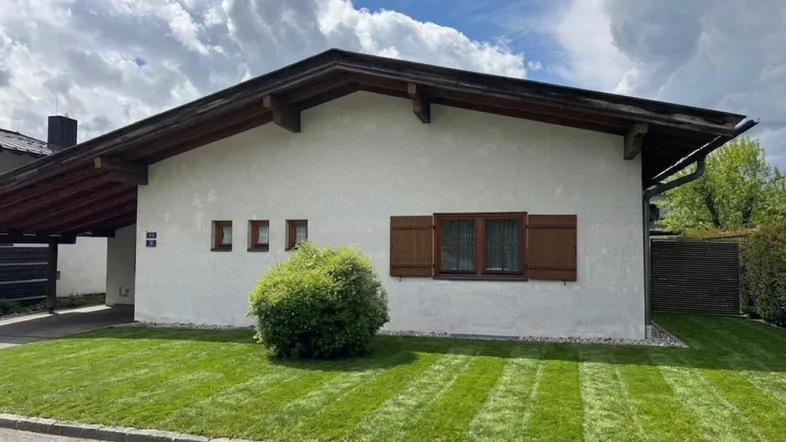 Charmantes Einfamilienhaus mit gepflegtem Rasen, Holzfensterläden und Carport.