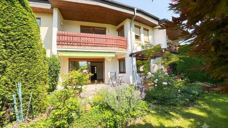 Gepflegter Gartenbereich mit Terrasse und Balkon, umgeben von üppigem Grün und blühenden Pflanzen.