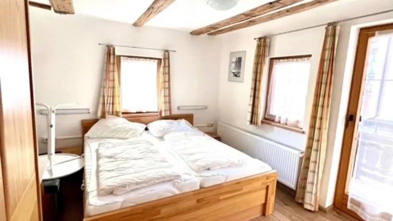 Gemütliches Schlafzimmer mit Holzbalken an der Decke, Holzboden und Zugang zu einem Balkon.