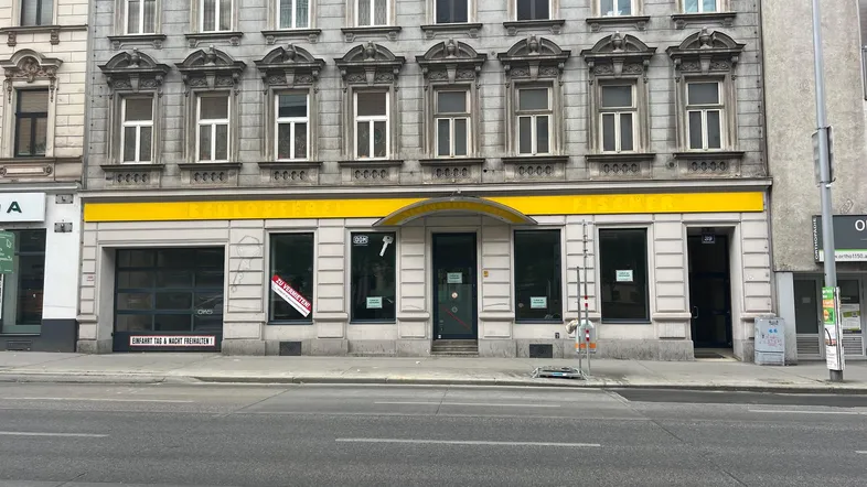 Historisches Gebäude mit reich verzierter Fassade und Gewerbeflächen im Erdgeschoss an einer belebten Straße.
