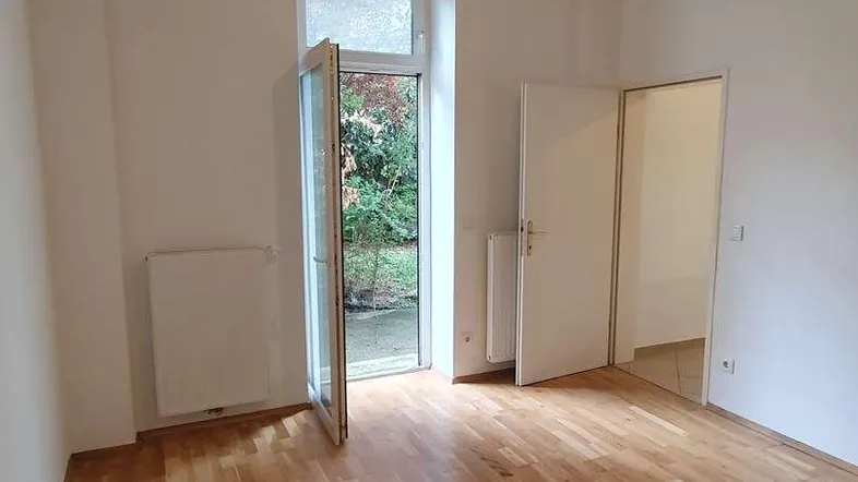 Helles Zimmer mit Holzboden und Zugang zu einem kleinen Außenbereich, ideal als Wohn- oder Schlafzimmer.