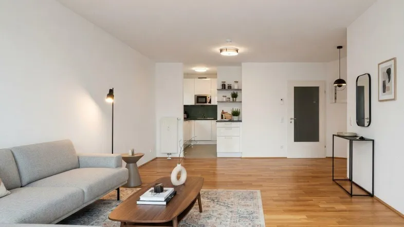 Helles Wohnzimmer mit Parkettboden, moderner Einrichtung und Blick auf die offene Küche.