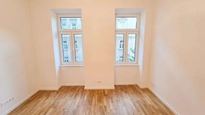 Geräumiges Zimmer mit zwei großen Fenstern und hellem Parkettboden, ideal für Wohn- oder Schlafbereich.