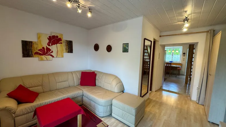 Gemütliches Wohnzimmer mit beigefarbenem Ecksofa, Holzboden und Deckenpaneelen, ideal zum Entspannen.