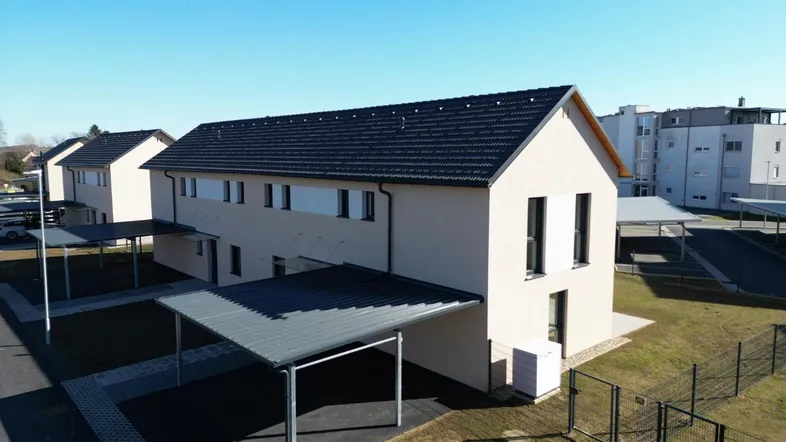 Moderne Reihenhäuser mit Carports und gepflegten Außenanlagen unter blauem Himmel.