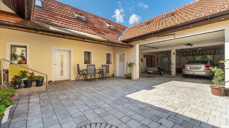 Gepflasterter Innenhof mit Sitzgelegenheiten und integrierter Doppelgarage unter blauem Himmel.