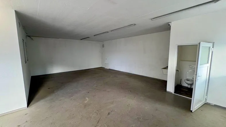 Geräumiger, leerer Gewerberaum mit Betonboden und integriertem Toilettenbereich, ideal für verschiedene Nutzungen.