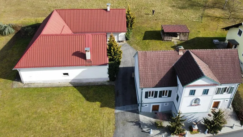 Luftaufnahme zweier Häuser mit roten Dächern und weitläufiger grüner Umgebung unter blauem Himmel.
