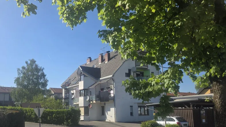 Mehrfamilienhaus mit mehreren Balkonen und Carport, umgeben von Bäumen und Grünflächen.