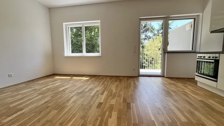 Helles Zimmer mit Holzboden, weißen Wänden und Zugang zu einem Balkon, bereit zum Einzug.