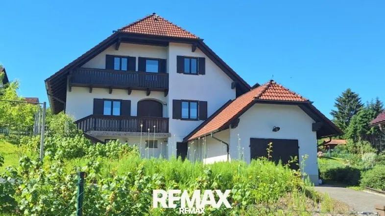 Traditionelles Einfamilienhaus mit Satteldach, Balkonen und integrierter Garage in ländlicher Umgebung.
