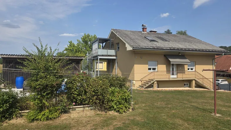 Hinteransicht des Hauses mit großem Garten und einer Außentreppe zum oberen Balkon.