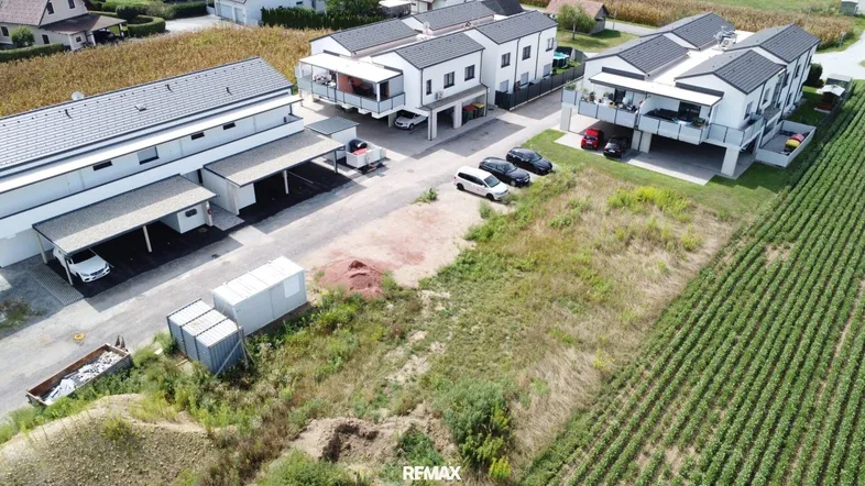 Luftaufnahme von modernen Wohngebäuden mit Carports und umliegenden Feldern in ländlicher Umgebung.