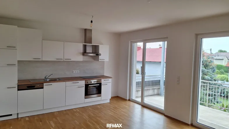 Moderne Einbauküche mit weißen Schränken, Holzarbeitsplatte und Zugang zu einem Balkon.